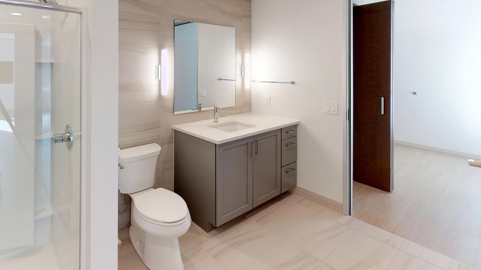 Elegant apartment bathroom at The Pressman Apartments in downtown Madison featuring Italian tile, a glass shower, and modern fixtures.