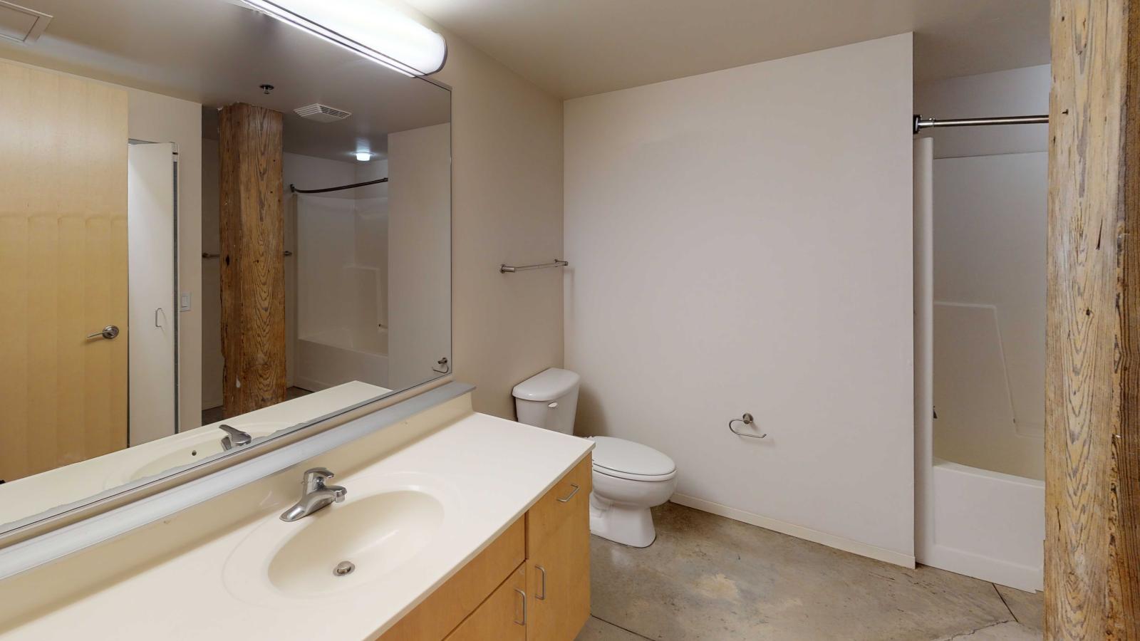 Spacious bathroom with contemporary vanity and soft industrial finishes in a one-bedroom at Tobacco Lofts