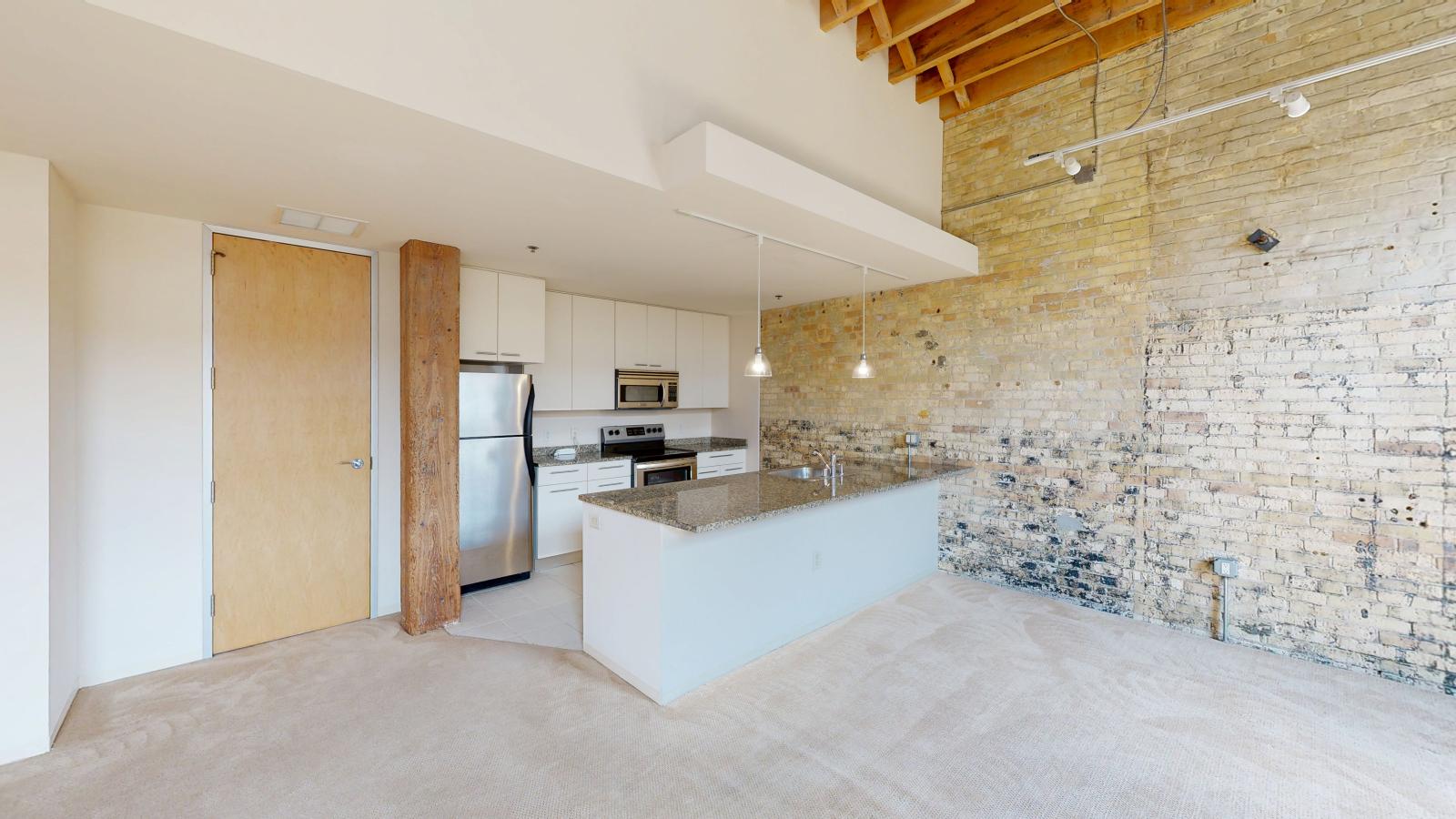 One bedroom apartment with an industrial style kitchen featuring granite countertops, and exposed brick, at Tobacco Lofts at The Yards in downtown Madison