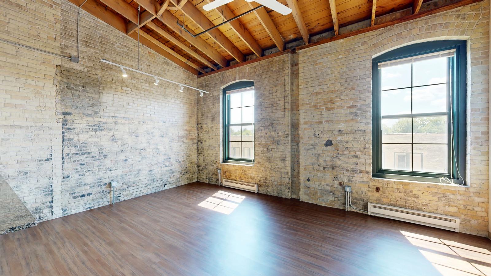 Modern one bedroom featuring exposed brick, large windows, and soft industrial finishes at Tobacco Lofts at The Yards in downtown Madison