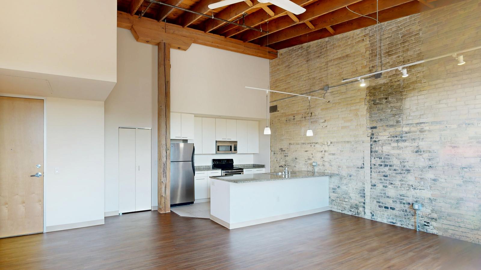 One bedroom apartment with a modern kitchen featuring granite countertops, and exposed brick, at Tobacco Lofts at The Yards in downtown Madison