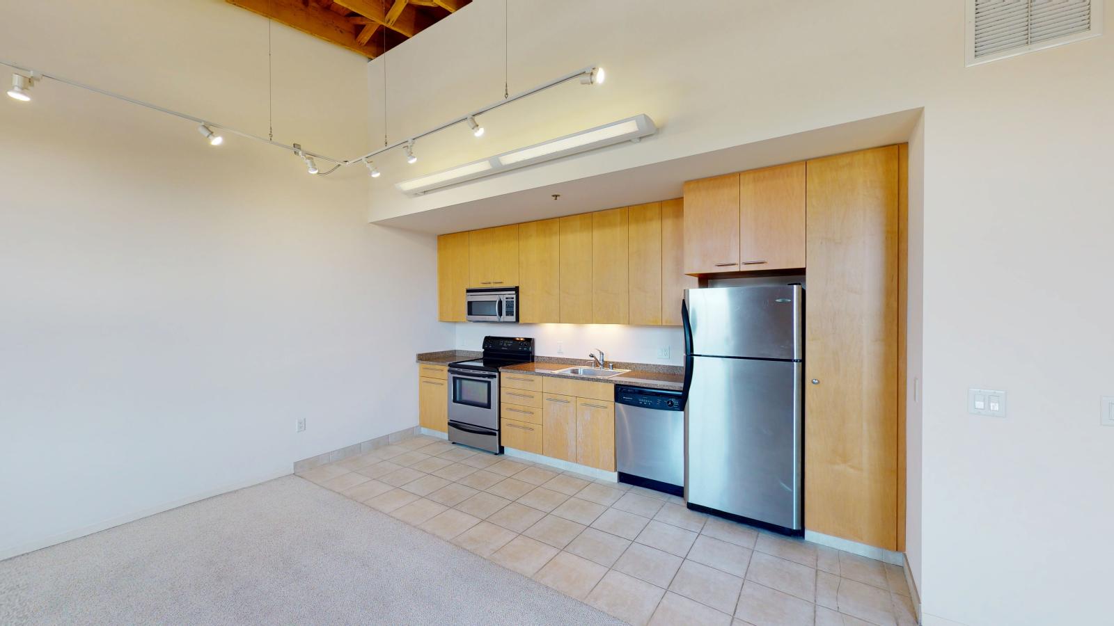 One bedroom apartment with a modern kitchen featuring granite countertops, and exposed brick, at Tobacco Lofts at The Yards in downtown Madison