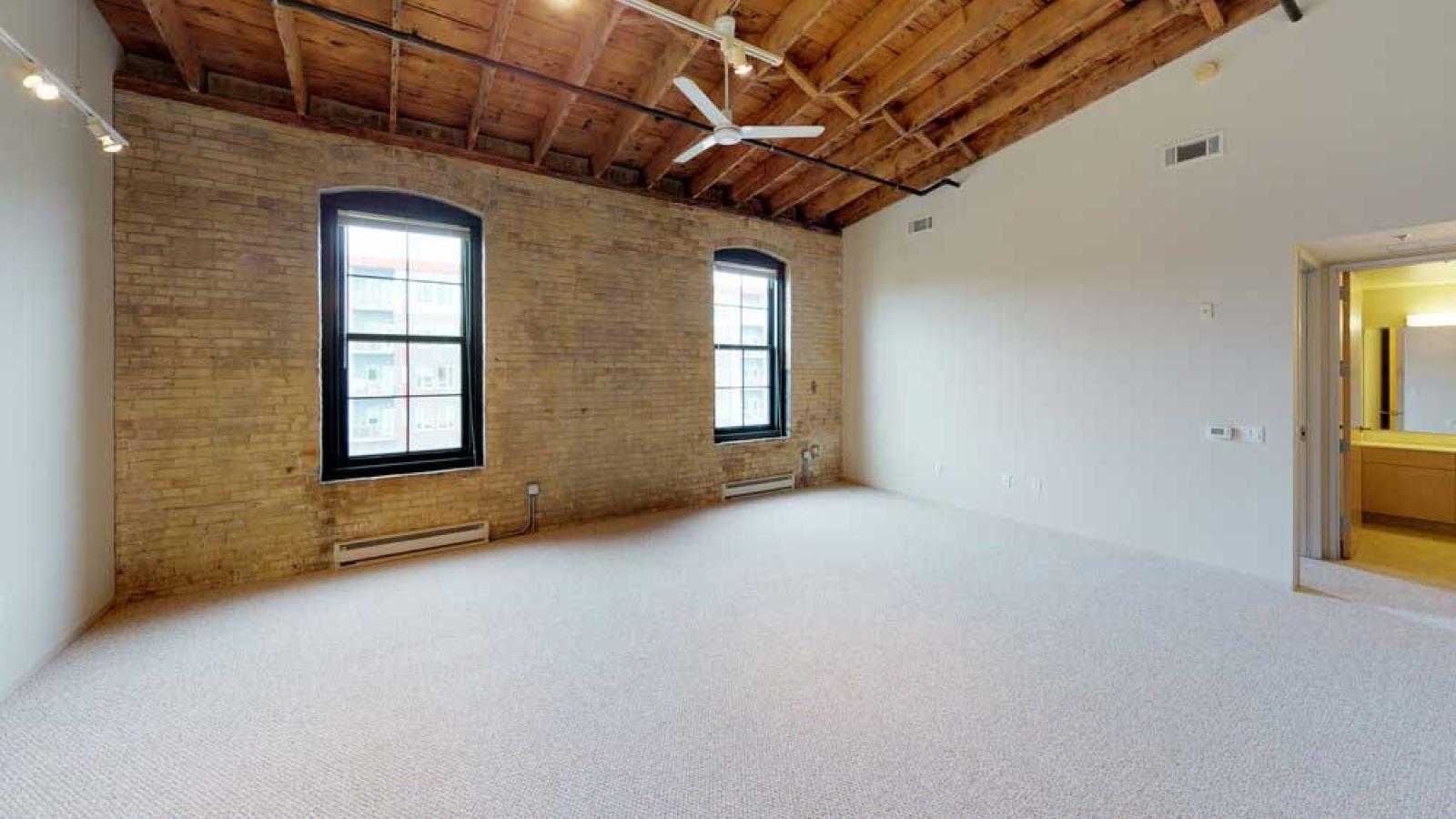 One bedroom featuring exposed brick, large windows, and soft industrial finishes at Tobacco Lofts