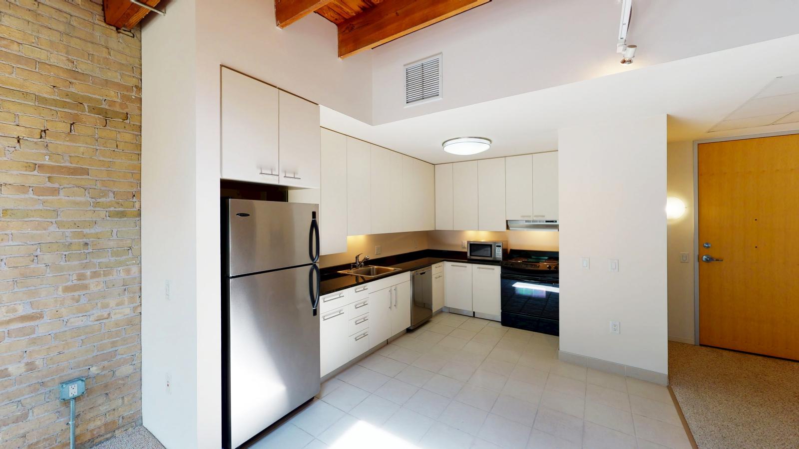 One bedroom apartment with an open-concept kitchen, modern appliances, and exposed brick at Tobacco Lofts at The Yards in downtown Madison