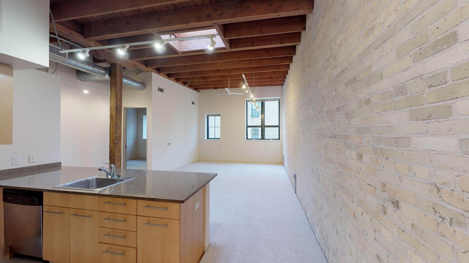 One bedroom apartment with an industrial style kitchen featuring granite countertops, and exposed brick, at Tobacco Lofts