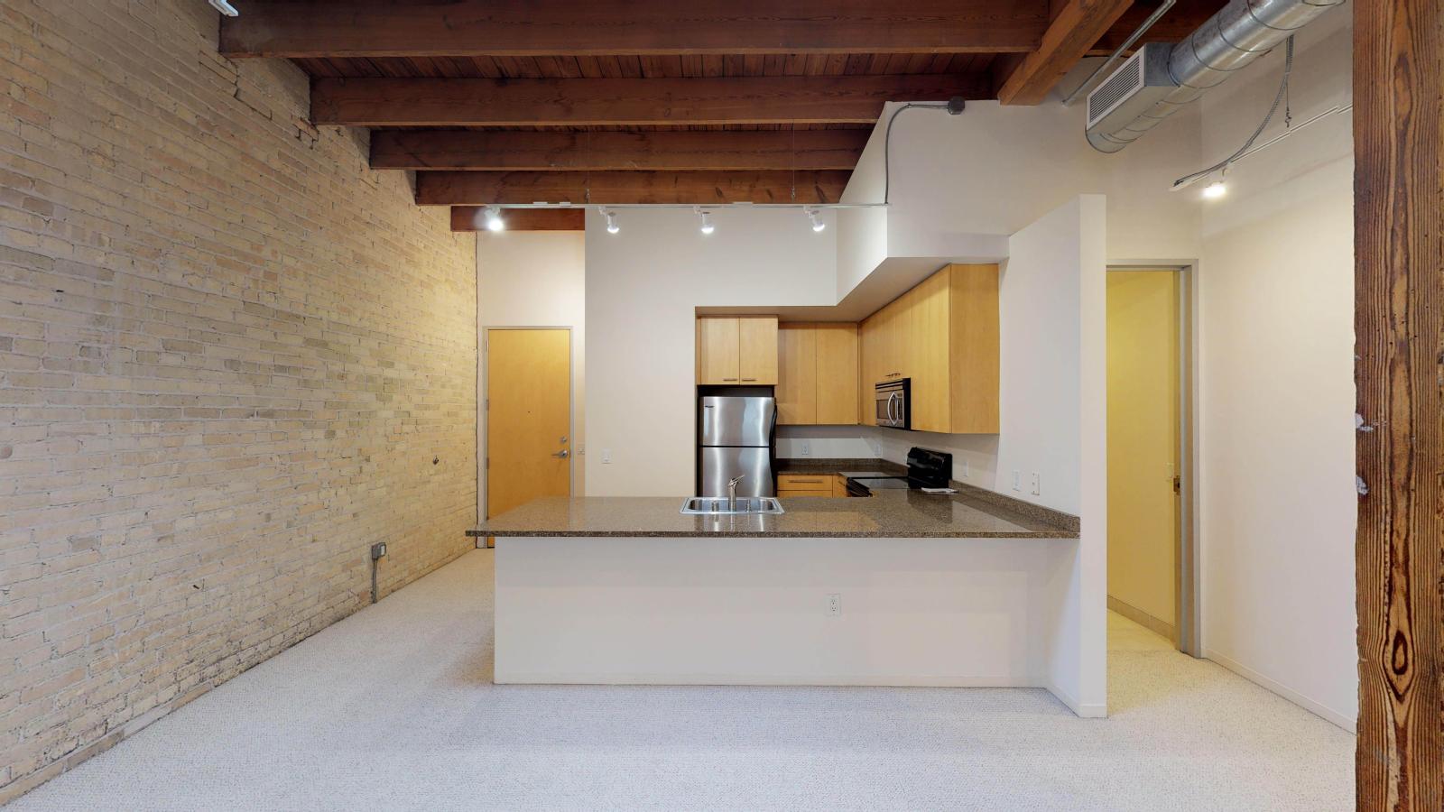 One bedroom apartment with an industrial style kitchen featuring granite countertops, and exposed brick, at Tobacco Lofts