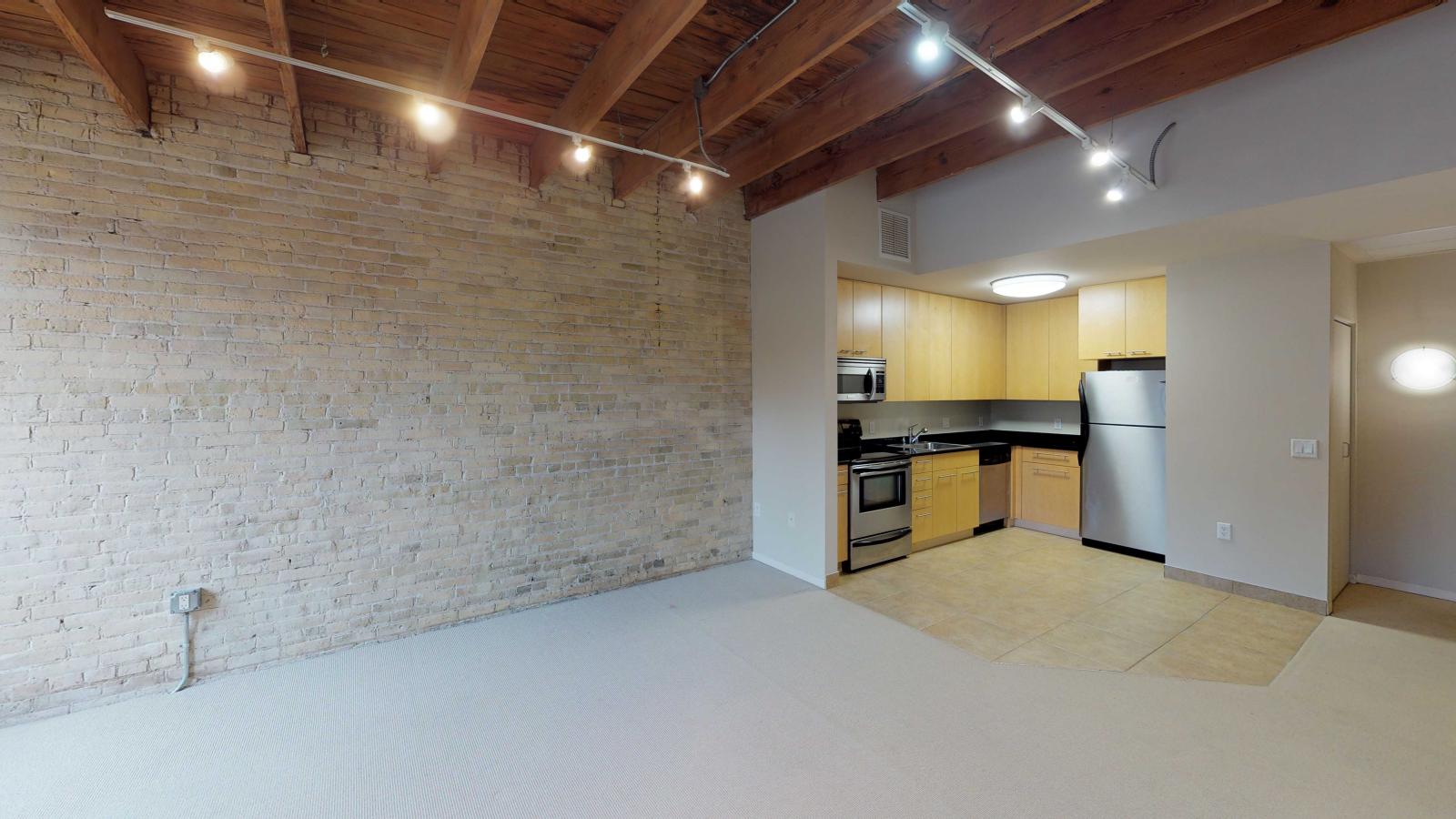 Studio apartment with an open-concept kitchen, modern appliances, and exposed brick at Tobacco Lofts