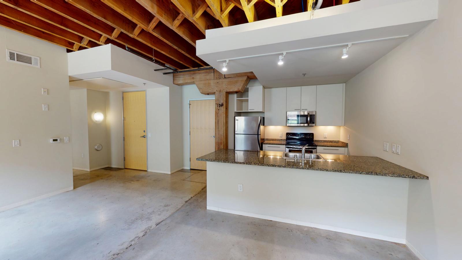 One bedroom apartment with an industrial style kitchen featuring granite countertops at Tobacco Lofts Apartment E108