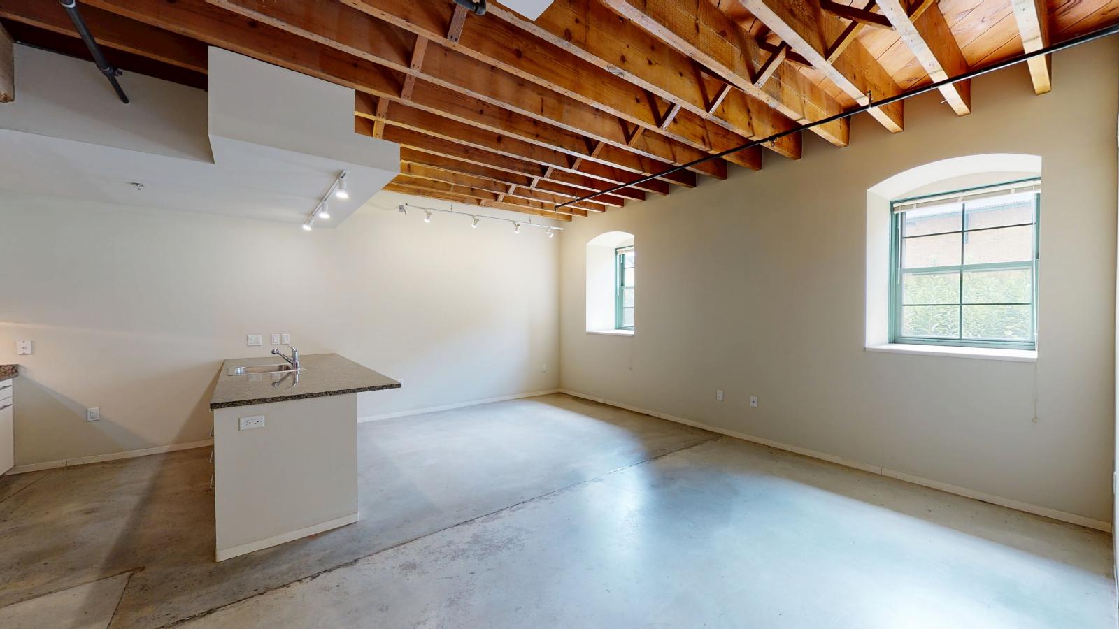 One bedroom with large windows, polished concrete flooring, and industrial style finishes at Tobacco Lofts Apartment E108