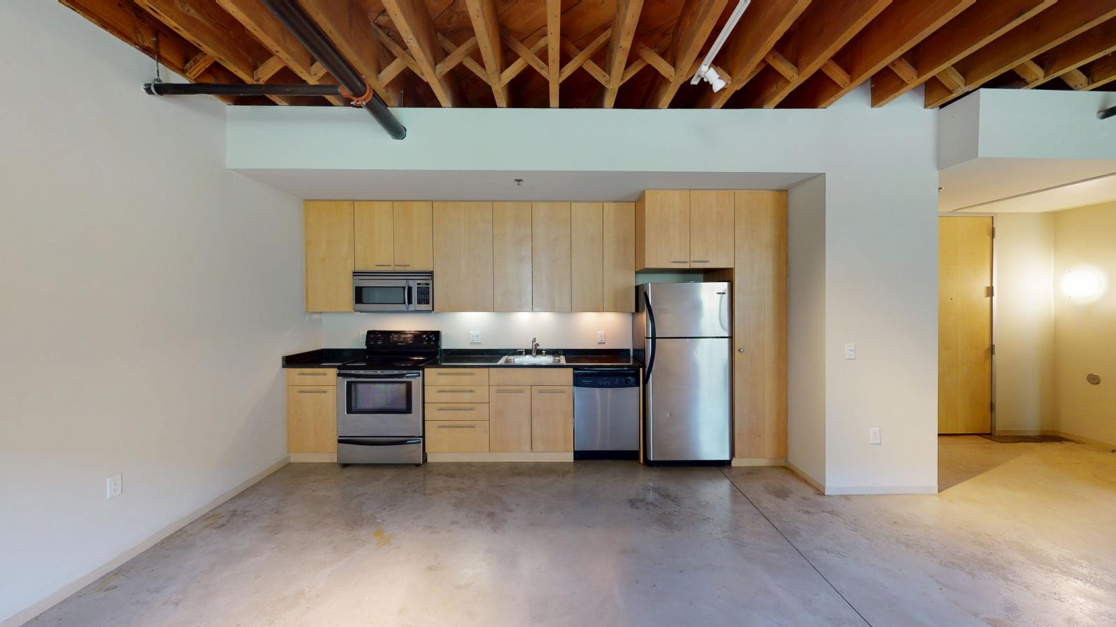 One bedroom apartment with an industrial style kitchen featuring granite countertops at Tobacco Lofts Apartment E108