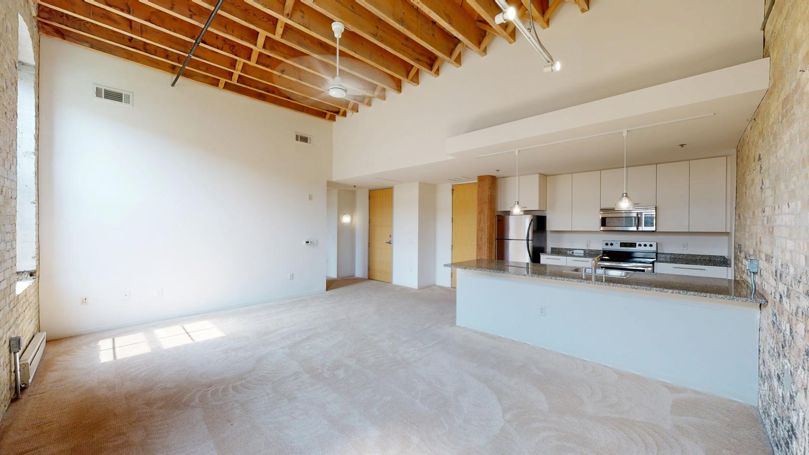 One bedroom apartment with an industrial style kitchen featuring granite countertops, and exposed brick, at Tobacco Lofts at The Yards in downtown Madison