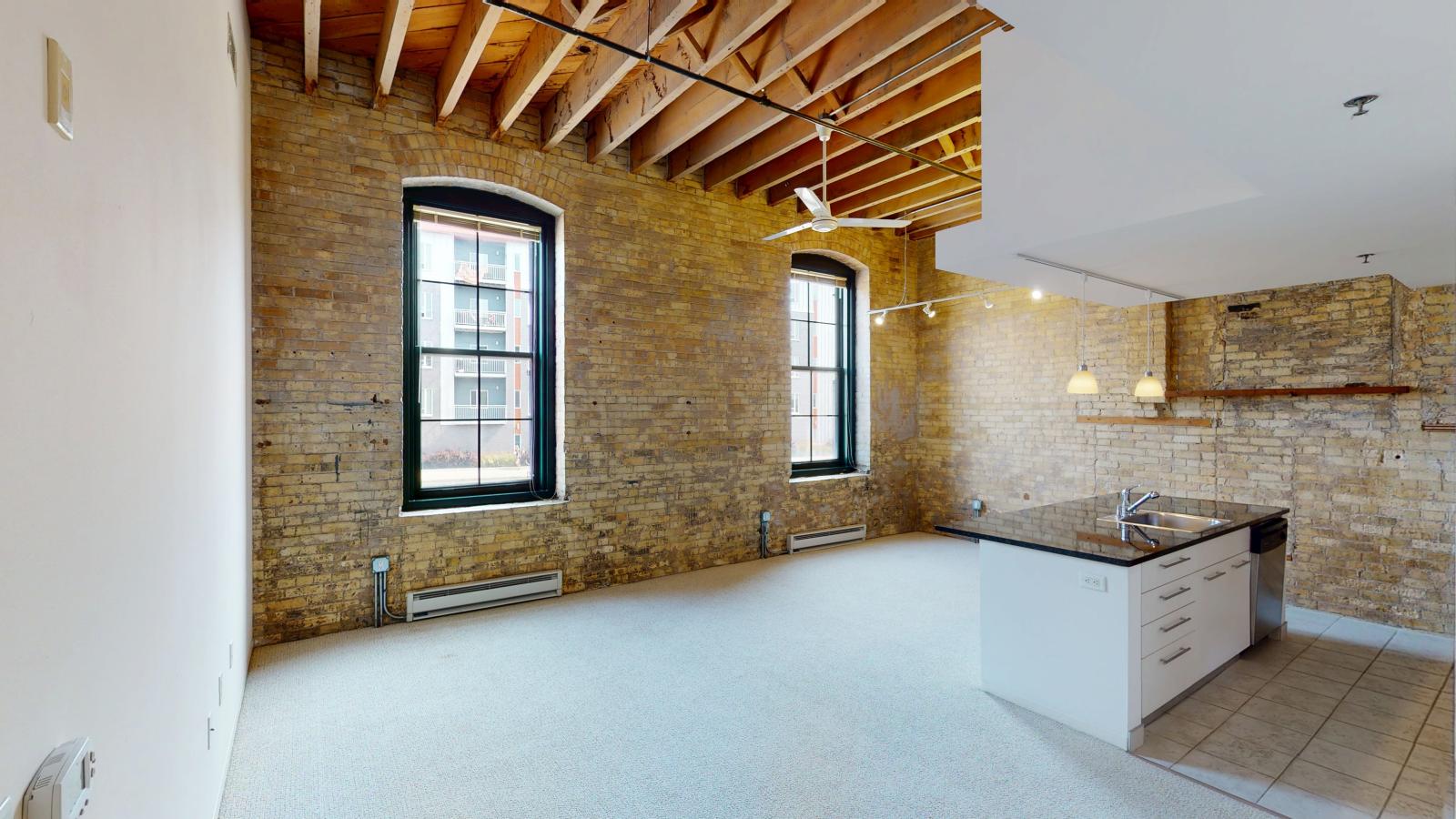 One bedroom apartment with an industrial style kitchen featuring granite countertops, and exposed brick, at Tobacco Lofts at The Yards in downtown Madison