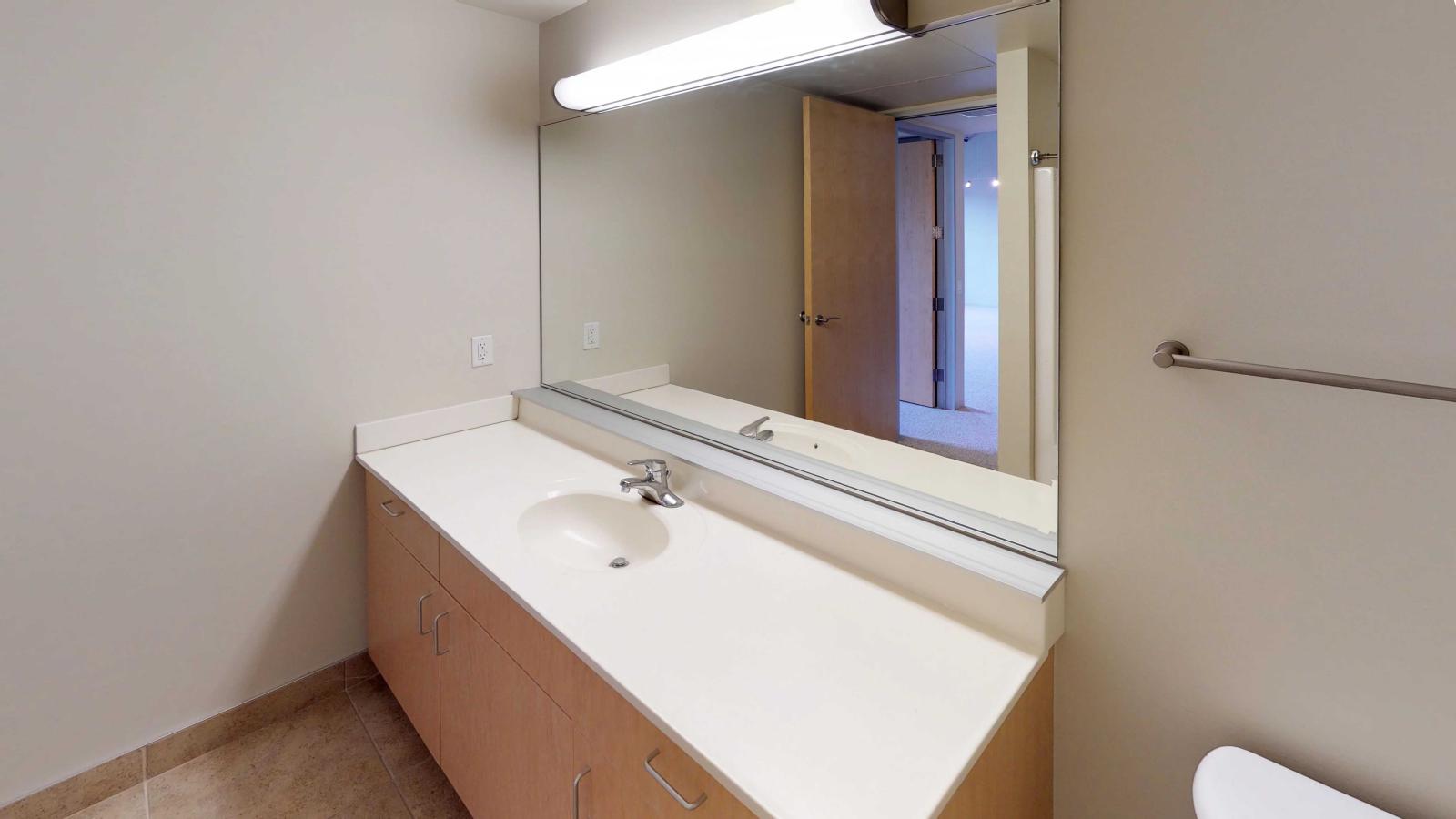 Spacious bathroom with contemporary vanity and soft industrial finishes in a one bedroom at Tobacco Lofts