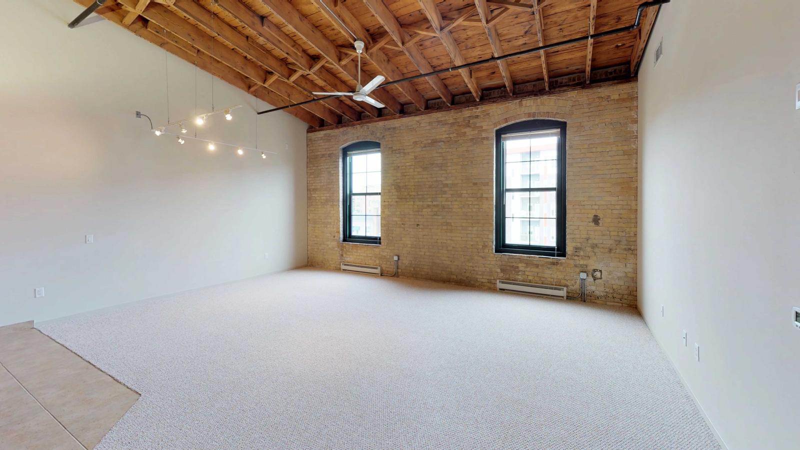 One bedroom featuring exposed brick, large windows, and soft industrial finishes at Tobacco Lofts
