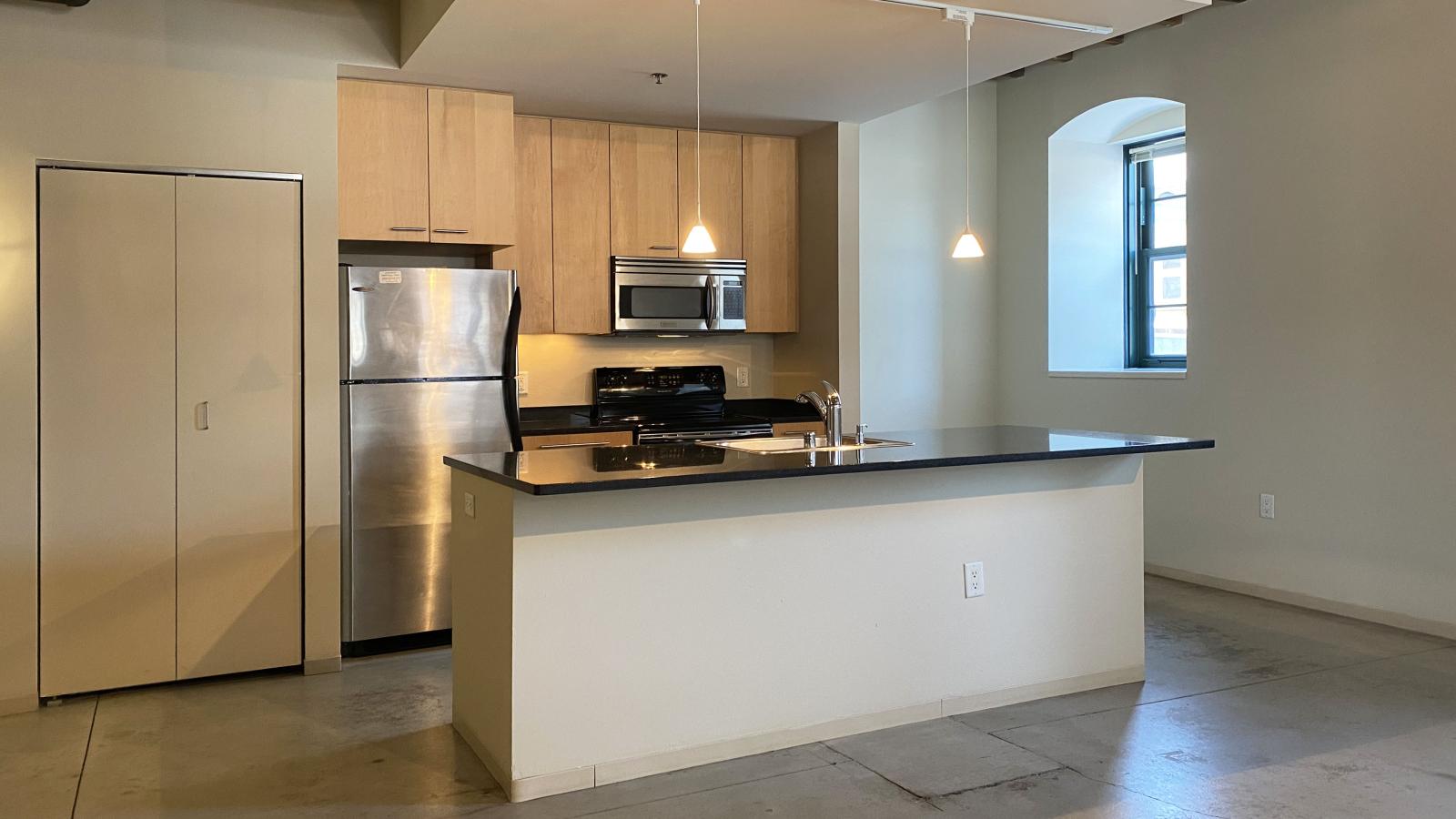 One bedroom apartment with an industrial style kitchen featuring granite countertops at Tobacco Lofts