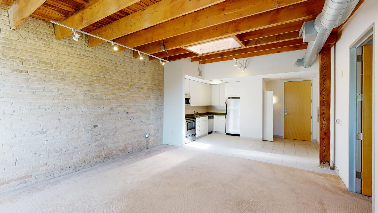 One bedroom apartment with a modern kitchen featuring granite countertops, and exposed brick, at Tobacco Lofts at The Yards in downtown Madison