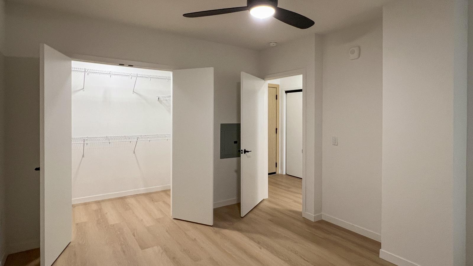 Modern bedroom at The Irwin Apartments with walk-in closet, black ceiling fan, luxury vinyl flooring, and contemporary finishes designed for comfortable downtown Madison living.