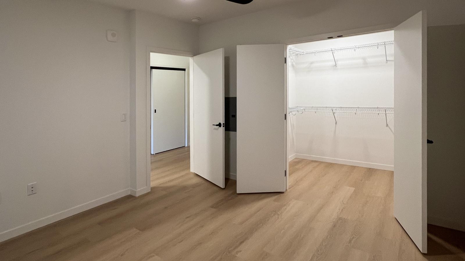 Modern apartment bedroom at The Irwin featuring walk-in closet, black ceiling fan, luxury vinyl flooring, and contemporary finishes in Madison’s Willy Street neighborhood.