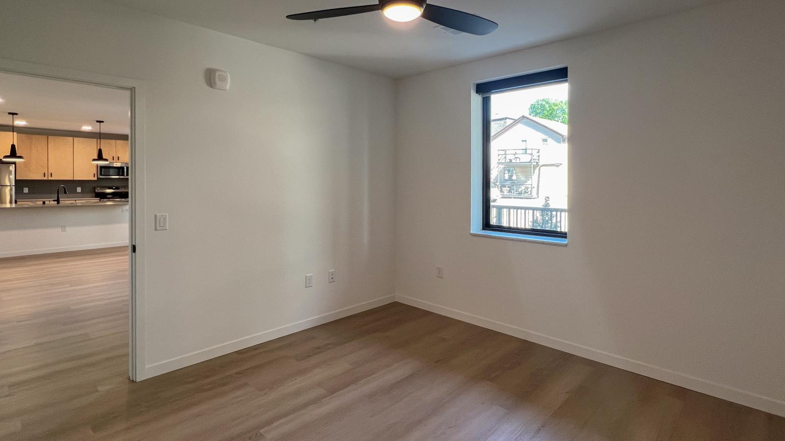 Bright modern bedroom at The Irwin Apartments featuring large black-framed windows, contemporary finishes, luxury vinyl flooring, ceiling fan, and connected open-concept layout in Madison, Wisconsin.