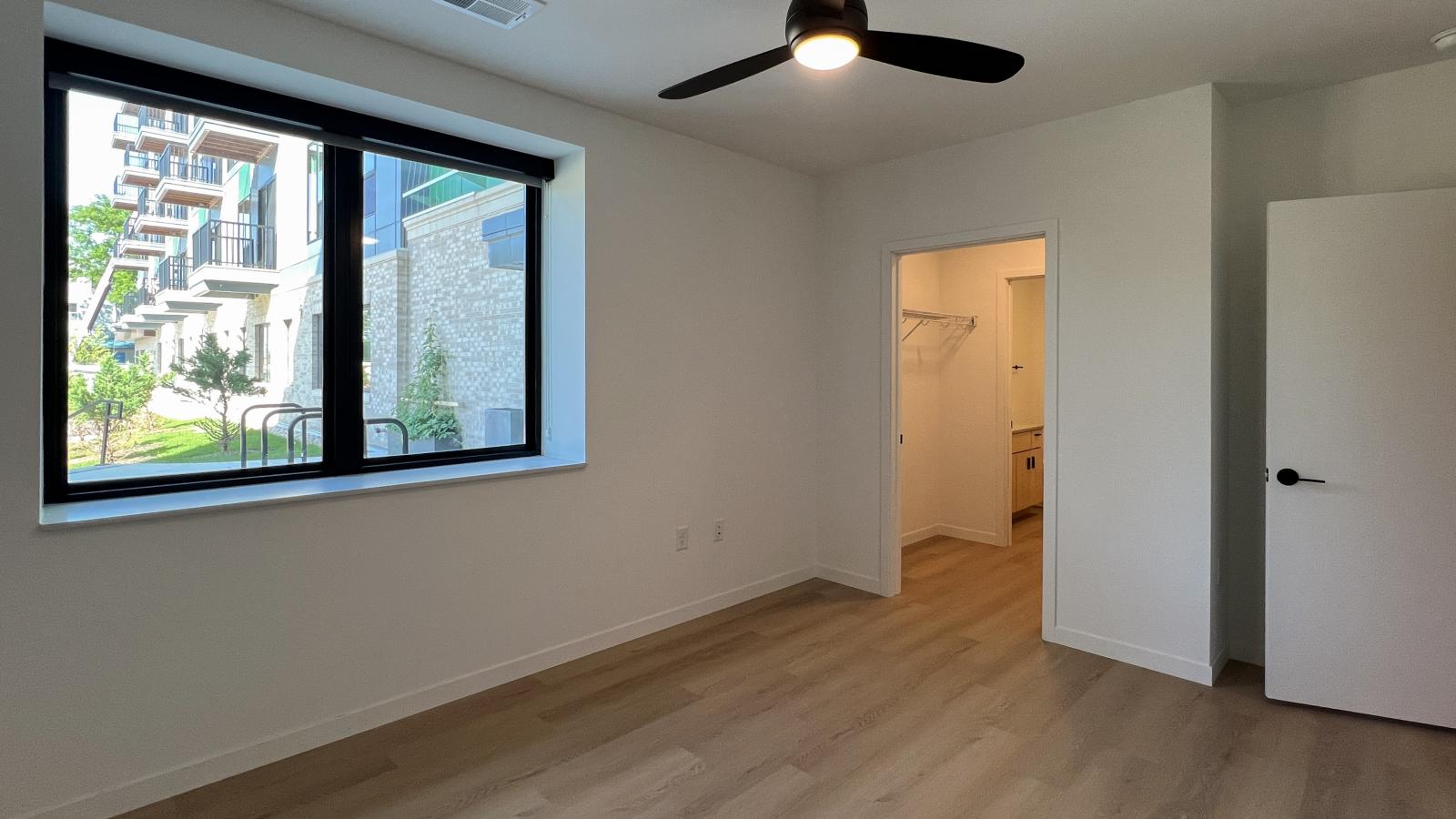 Modern two-bedroom apartment bedroom at The Irwin featuring oversized black-trim windows, ceiling fan, luxury vinyl flooring, natural light, and contemporary finishes in Madison’s Willy Street neighborhood.