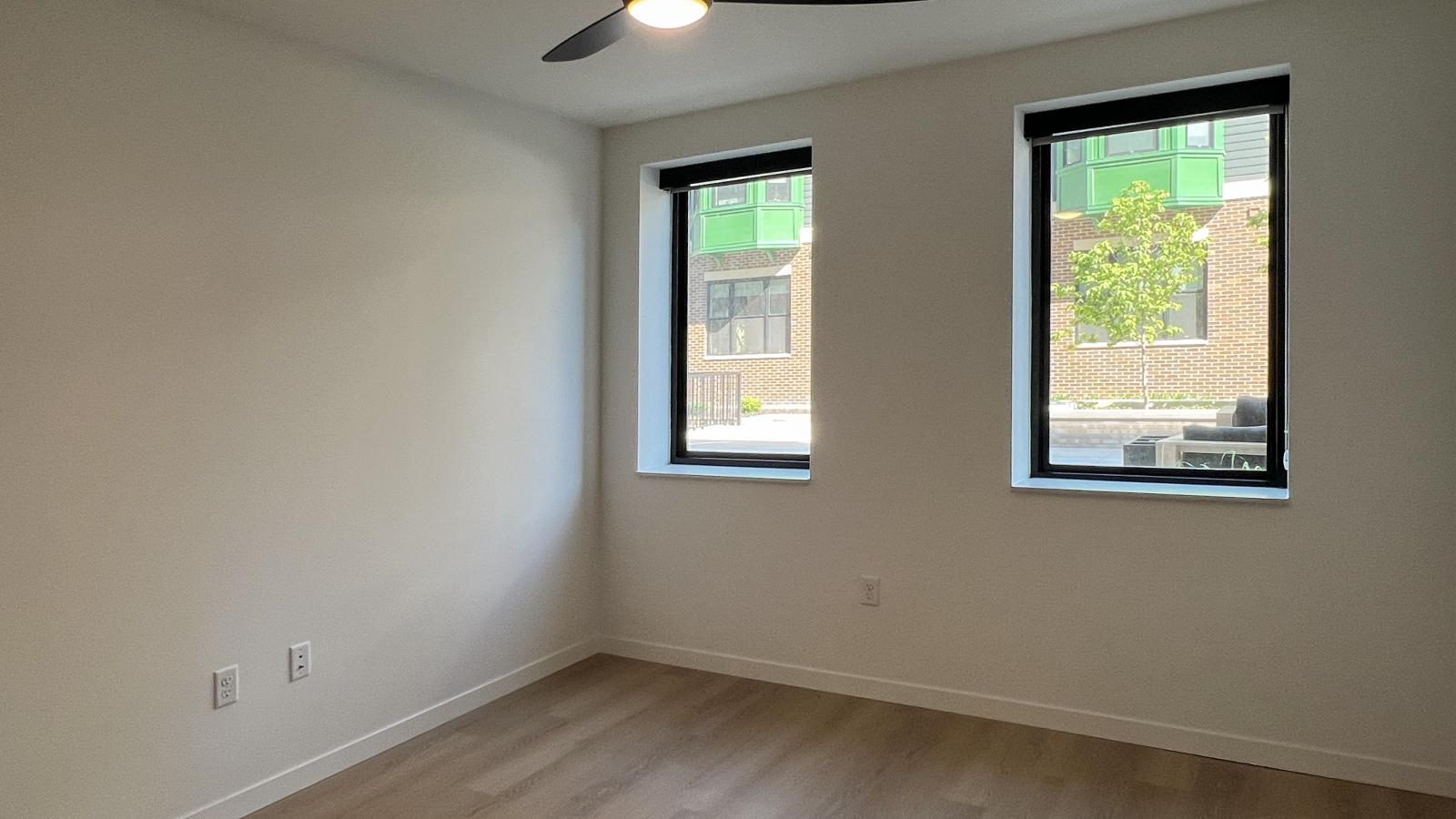 Modern apartment bedroom at The Irwin featuring oversized black-trim windows, ceiling fan, luxury vinyl flooring, and contemporary finishes in Madison’s Willy Street neighborhood.