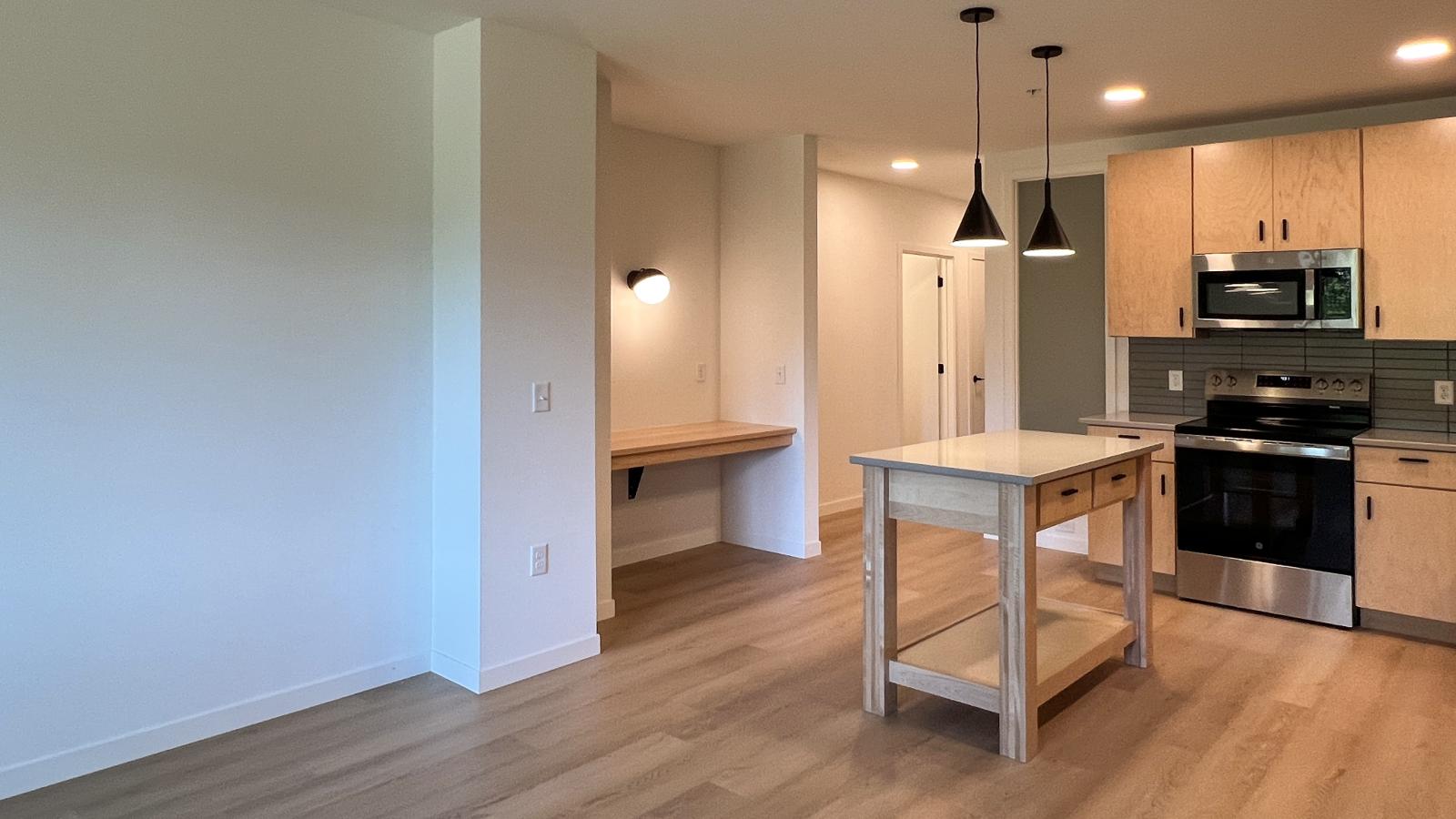 Open-concept kitchen and workspace area at The Irwin featuring built-in desk, modern cabinetry, kitchen island, stainless steel appliances, and luxury vinyl flooring in Madison’s Marquette neighborhood.