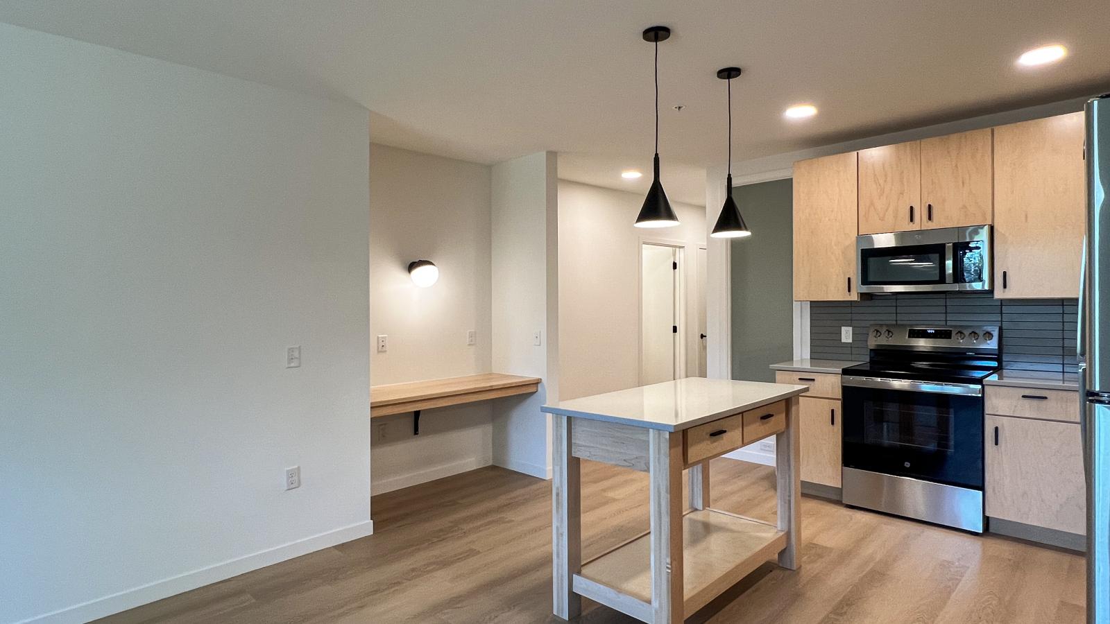 One bedroom apartment featuring a built in workspace and desk area adjacent to the open concept kitchen with natural wood cabinetry, pendant lighting, luxury vinyl plank flooring, and modern finishes in downtown Madison