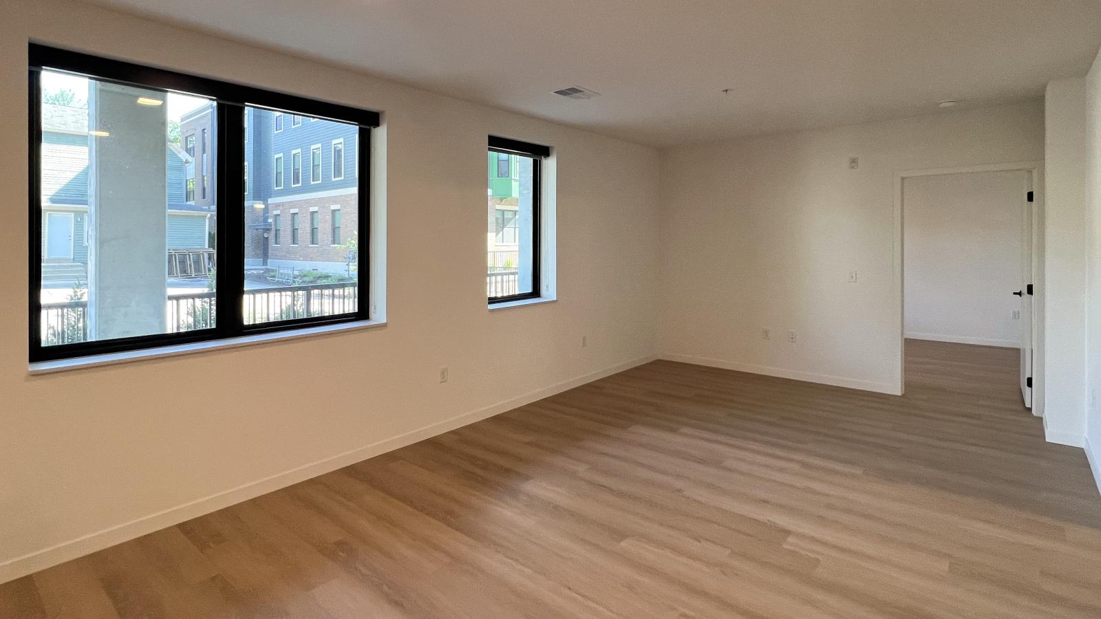 Spacious one-bedroom apartment living area at The Irwin with oversized black-trim windows, abundant natural light, luxury vinyl plank flooring, open layout, and modern minimalist finishes near downtown Madison.